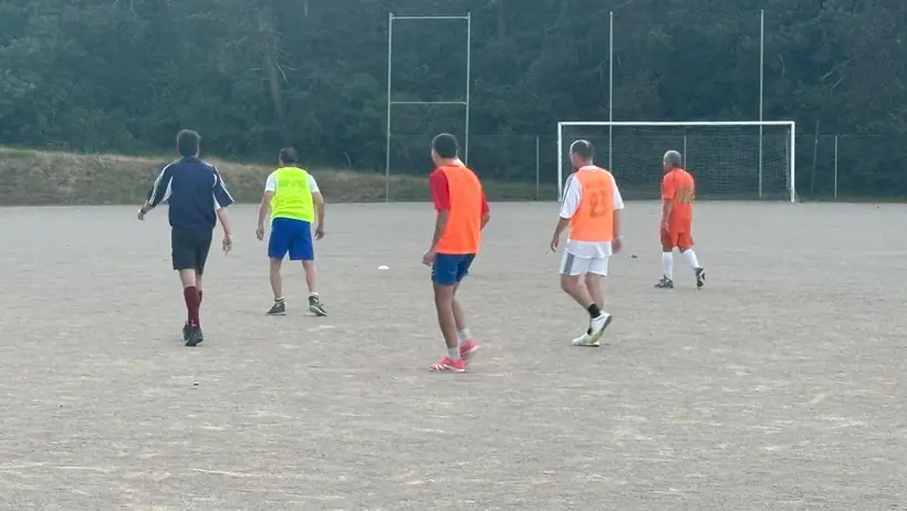 Match sur le terrain stabilisé, joueurs en chasubles orange et jaune